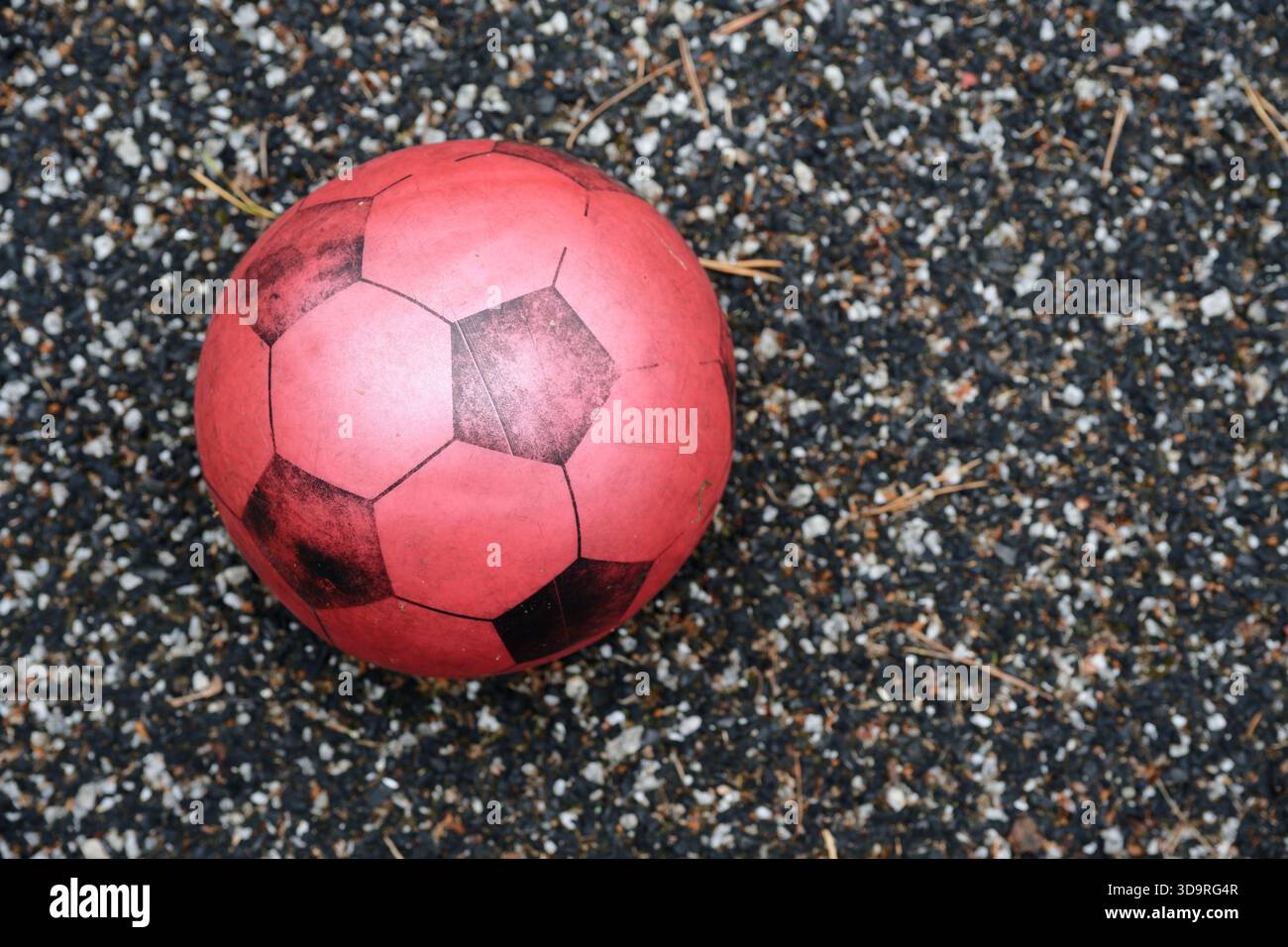 Un pallone da calcio leggero in gomma rossa con toppe nere si appoggia su un sentiero pavimentato in pietra, creando un vivace contrasto con la superficie naturale. Foto Stock