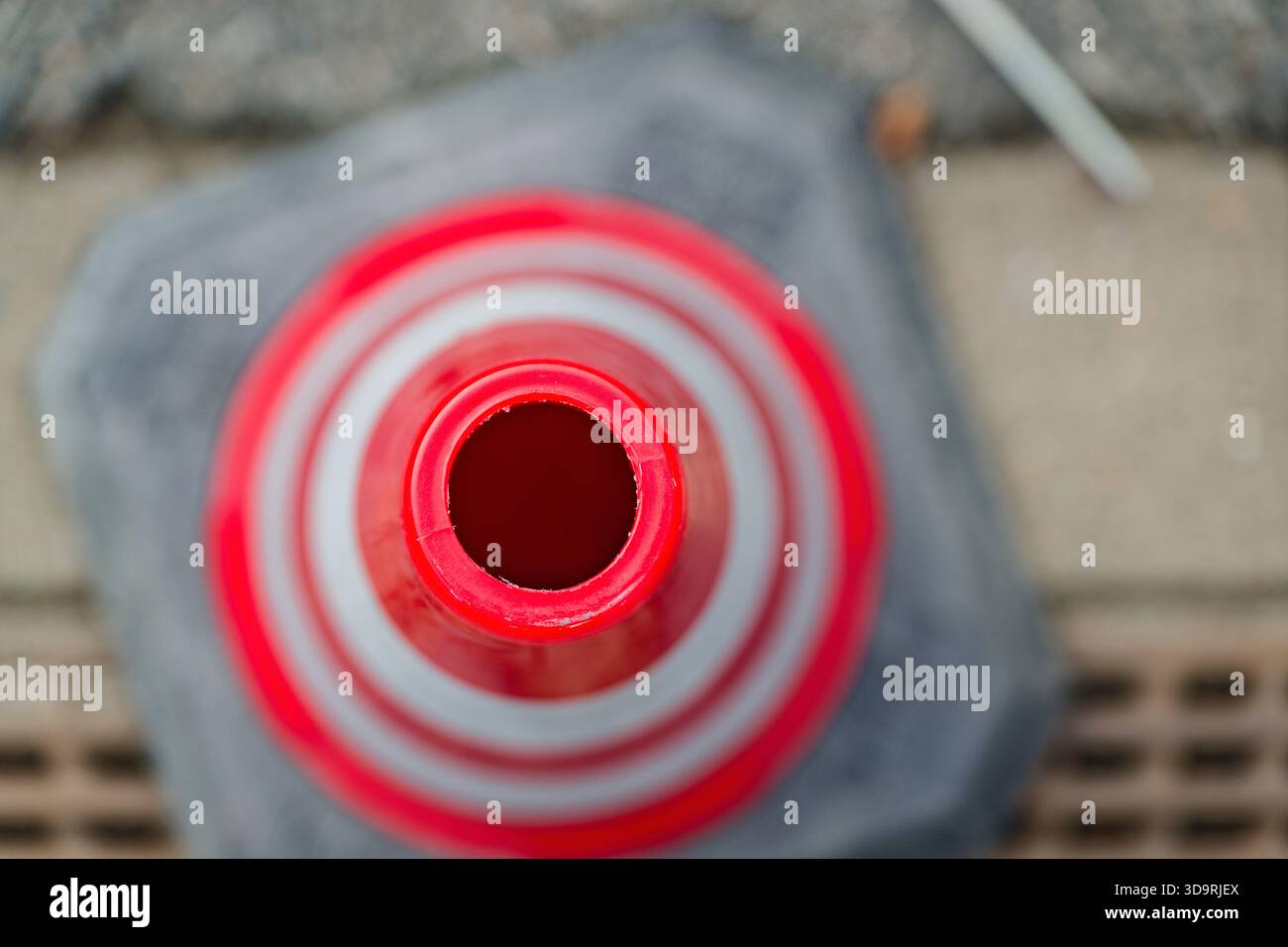 Vista ravvicinata di un cono rosso stradale con strisce bianche riflettenti che mostrano la parte superiore cava e la superficie ruvida. Lo sfondo è sfocato, enfatizzato Foto Stock