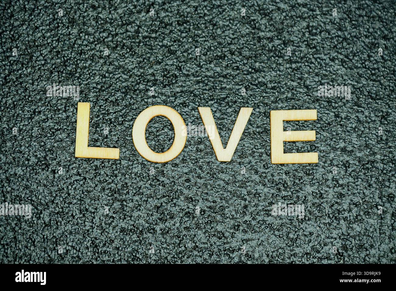 La parola "amore" è formata da lettere di legno poste su un tappetino in gomma nero con una texture sottile, offrendo una presentazione visiva chiara e creativa. Foto Stock