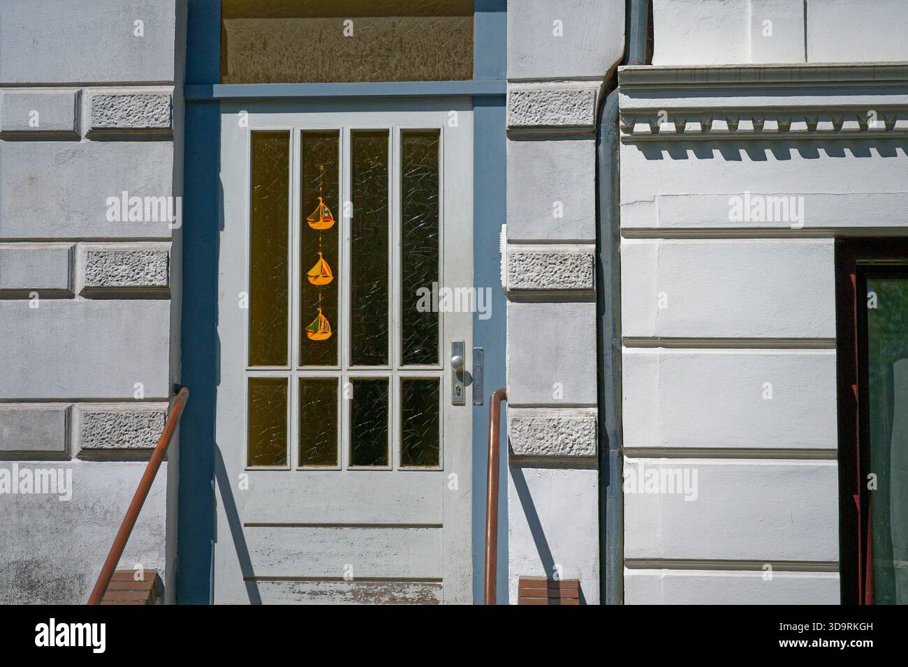 Una vecchia porta di legno bianca con pannelli di vetro gialli mostra segni di usura. All'interno sono appesi tre colorati campanili a forma di nave, che creano un affascinante e nos Foto Stock