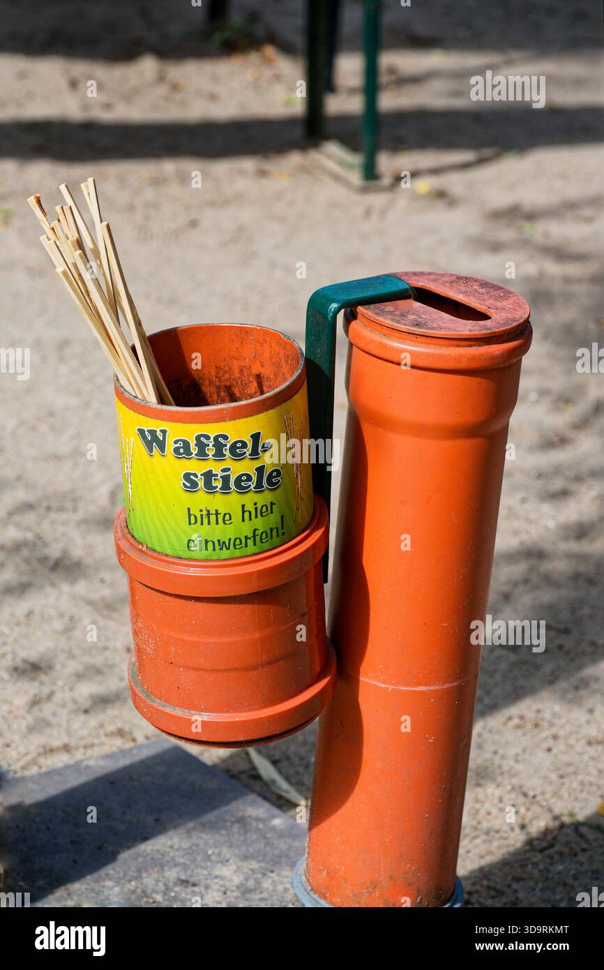 Un tubo di plastica verticale con un recipiente laterale contiene bastoncini di legno per lo smaltimento contrassegnati con il testo tedesco Waffelstiele bitte hier einwerfen che funge da A. Foto Stock