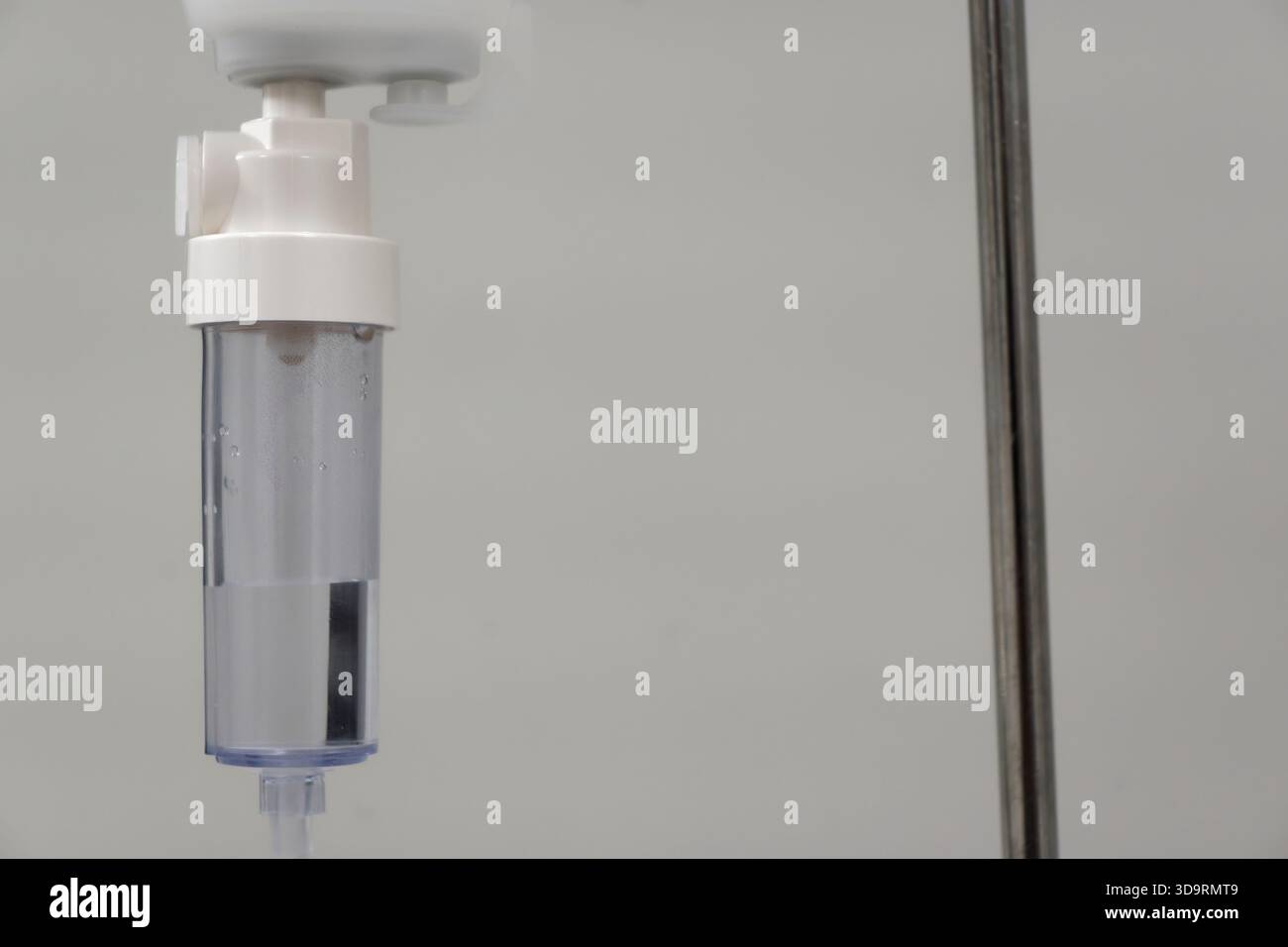 Un'infusione endovenosa gocciola costantemente da una camera trasparente fissata a un tappo bianco su un set appeso. L'unità è montata su un palo metallico lucido. Trasm Foto Stock