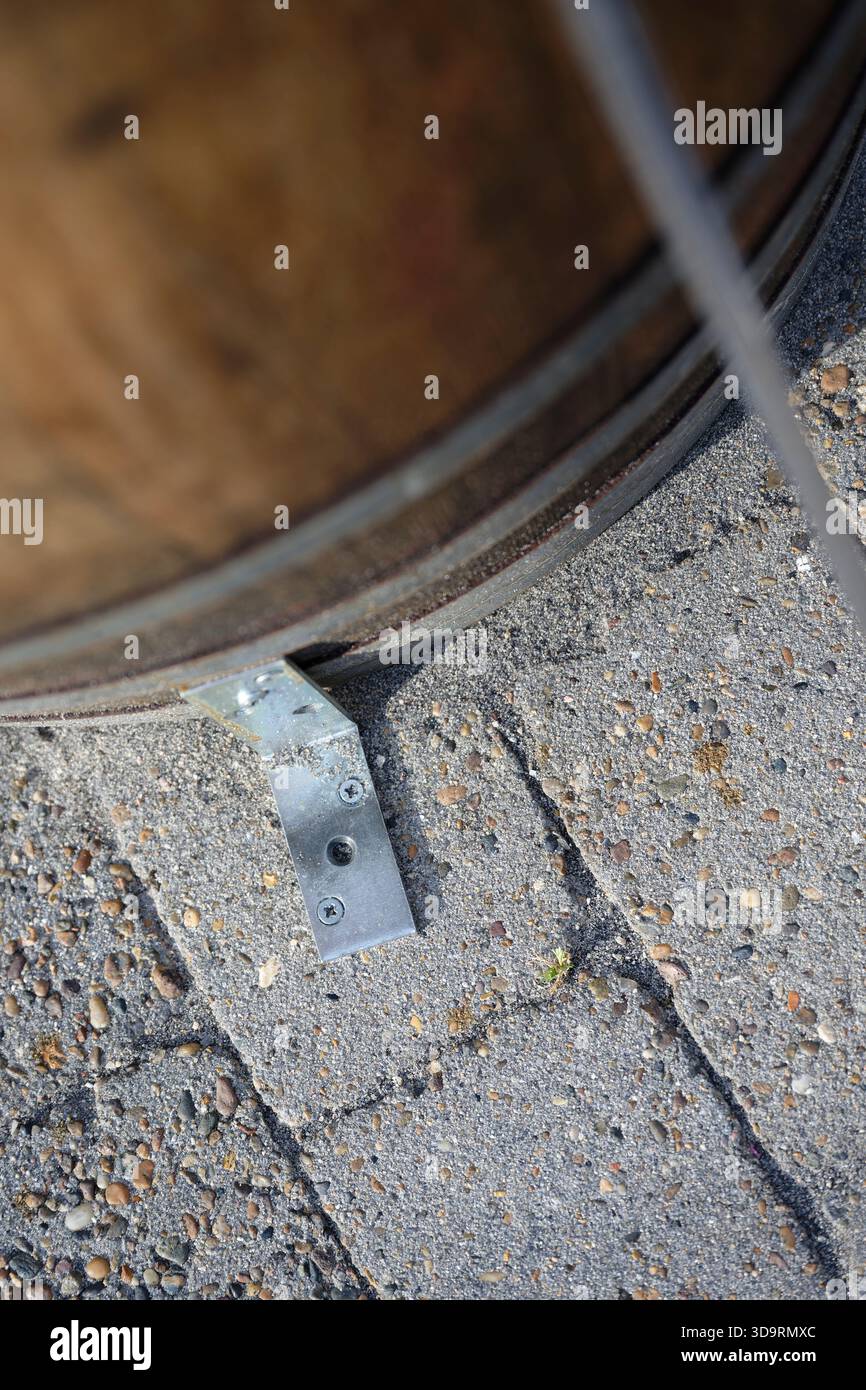 Un barile in legno con canaline metalliche è fissato a una piastra metallica su pavimentazione esterna. Le stave hanno un aspetto stagionato e scuro, le cinghie in ferro mostrano usura, ma Foto Stock