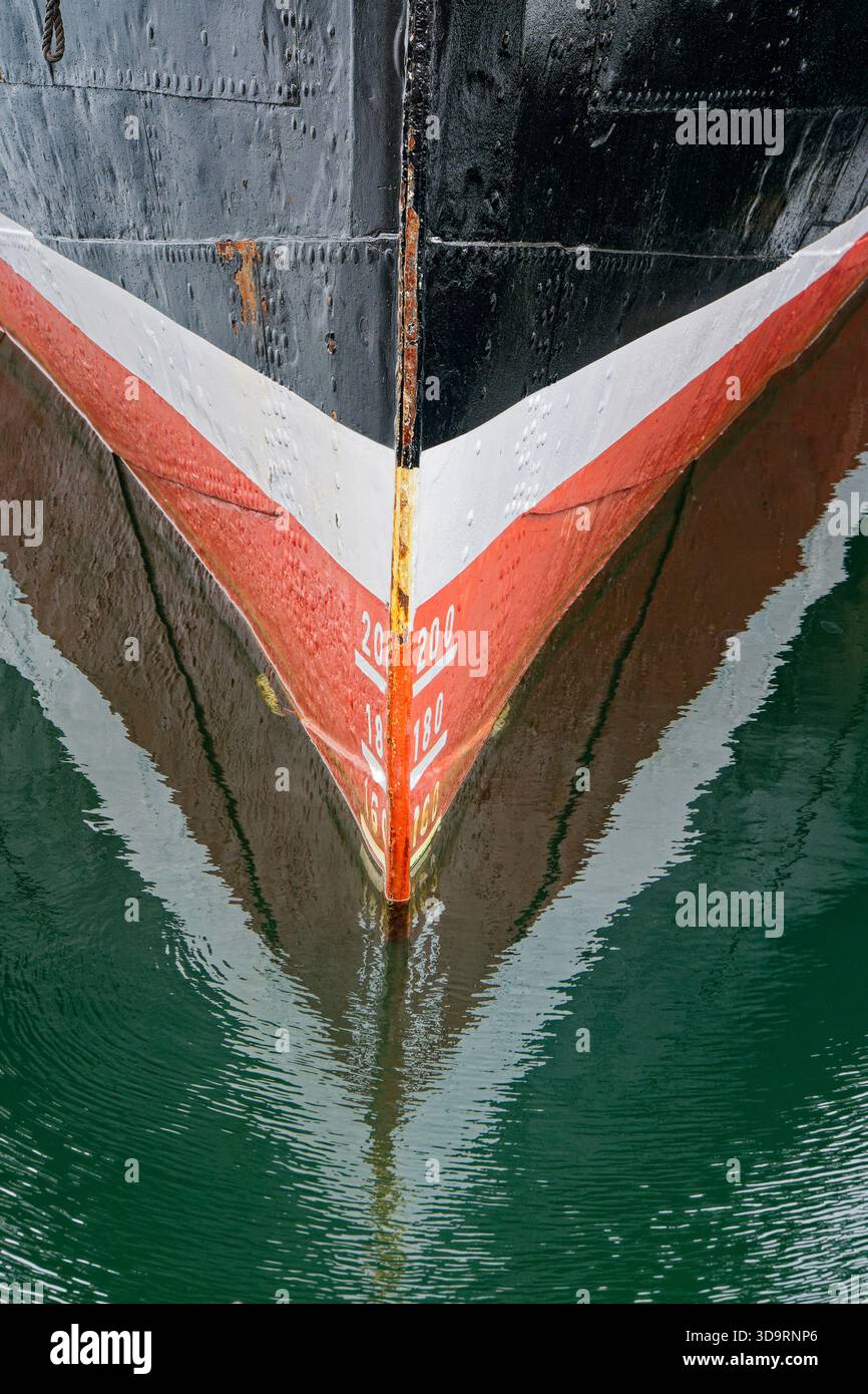 Un arco di acciaio nero si innalza sopra l'acqua calma. Una fascia bianca si trova su una striscia rossa, con piccoli fiori di ruggine. I segni di tiro 200, 180, 160 allineano il naso, misururi Foto Stock