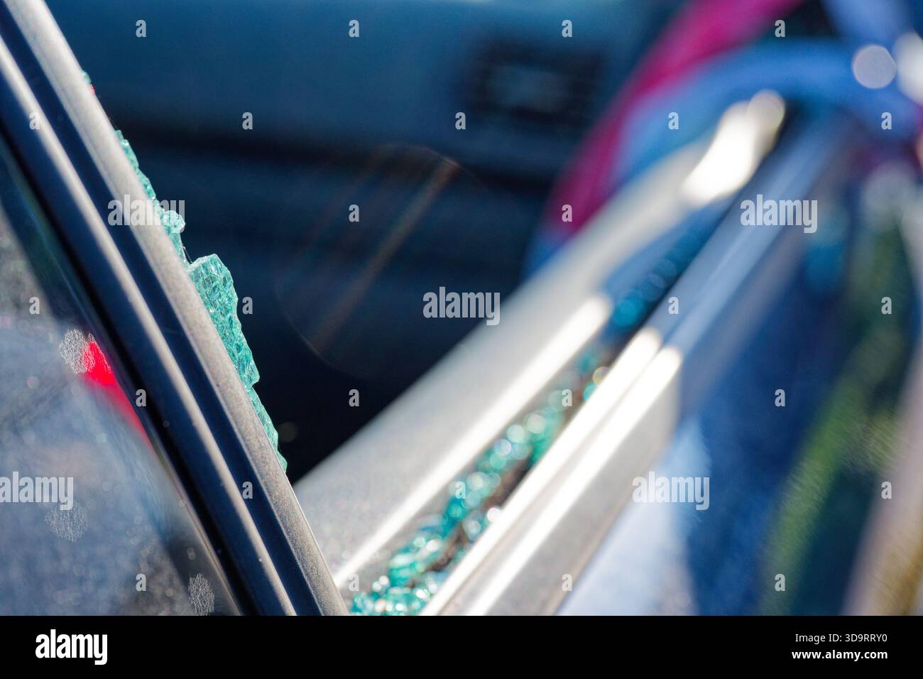 Un finestrino laterale è rotto e piccoli frammenti di vetro di sicurezza si trovano sul sedile e sul pavimento, pezzi scintillanti che si aggrappano al telaio e sigillano, l'auto attende c Foto Stock