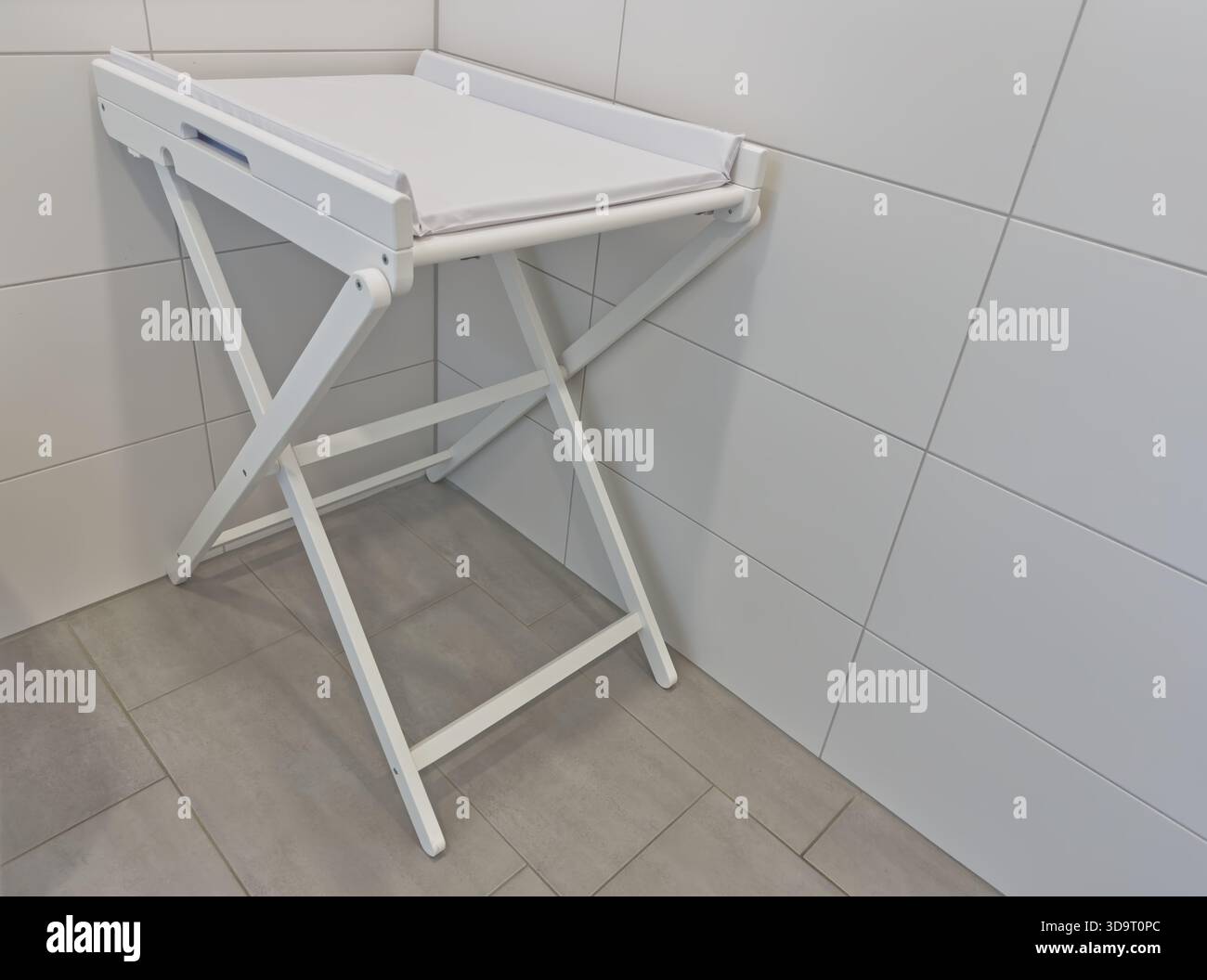 Uno spogliatoio pieghevole bianco posizionato contro una parete piastrellata in un bagno. Il tavolo presenta una superficie piana ed è supportato da un telaio robusto, di Foto Stock