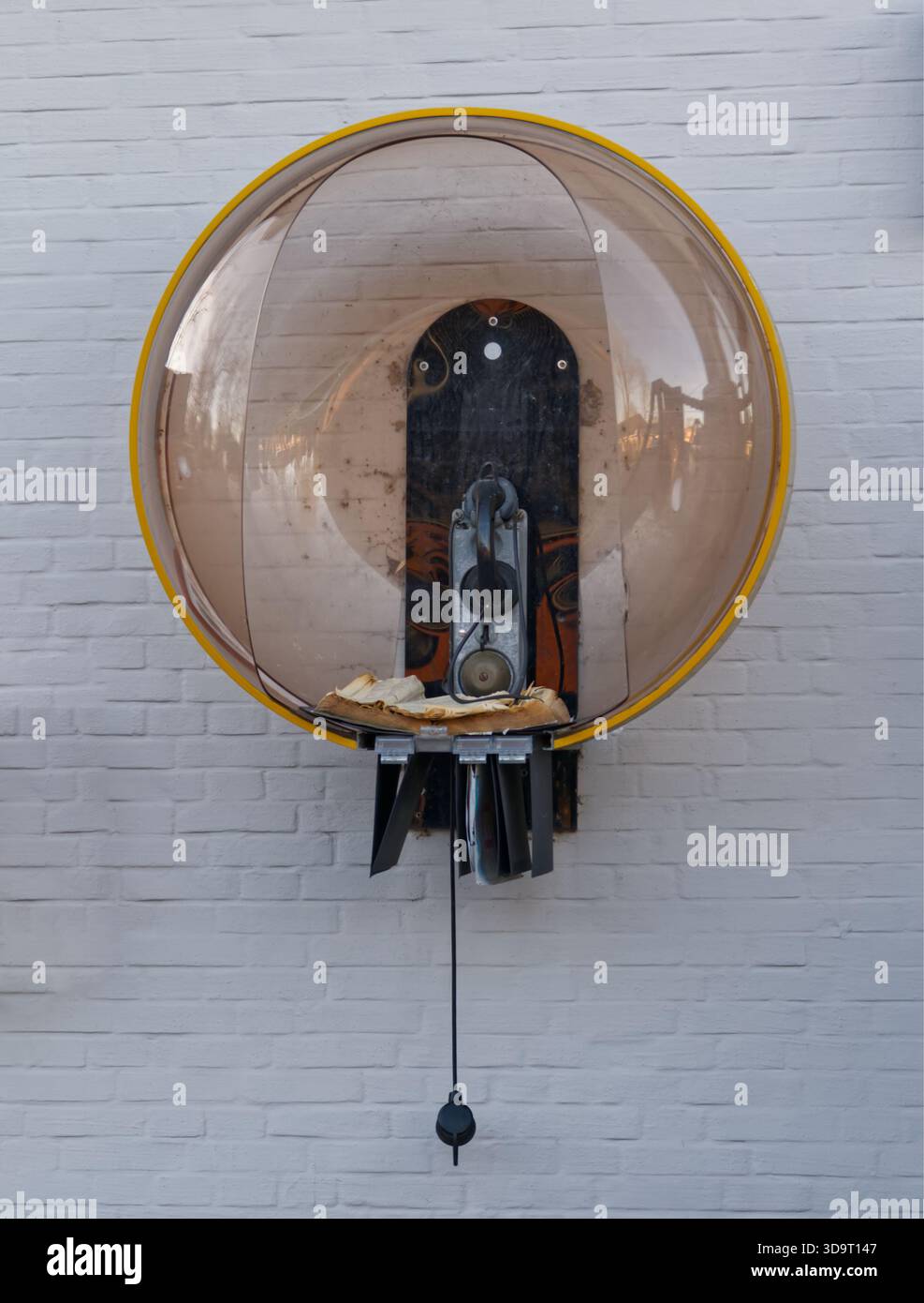 Un telefono pubblico retrò particolarmente elegante in una cupola trasparente su una parete, davanti a uno sfondo bianco in mattoni e un vecchio telefono aperto Foto Stock