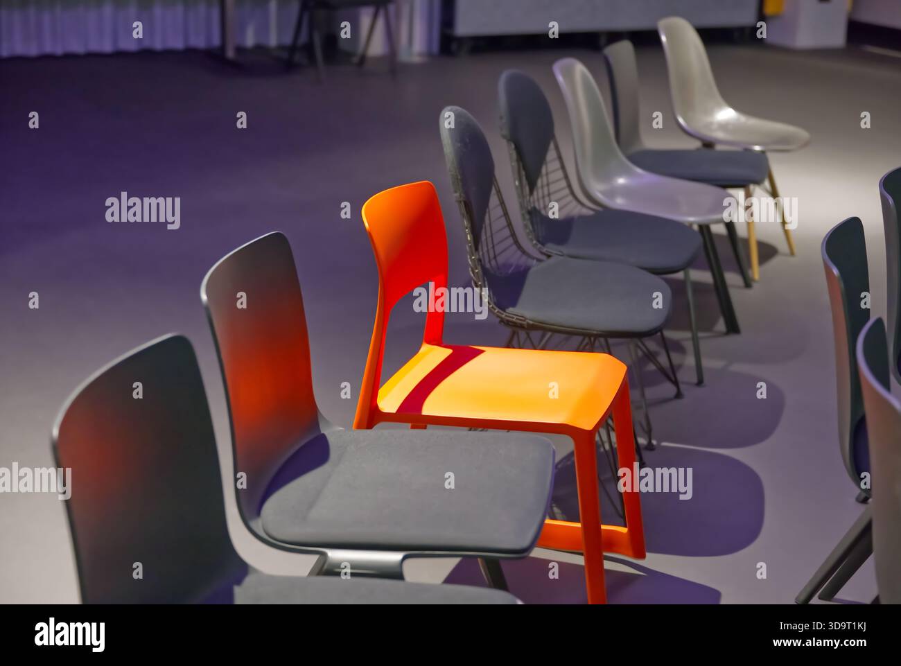Una fila di sedie moderne con una luminosa sedia arancione che si distingue tra quelle grigie. Foto Stock