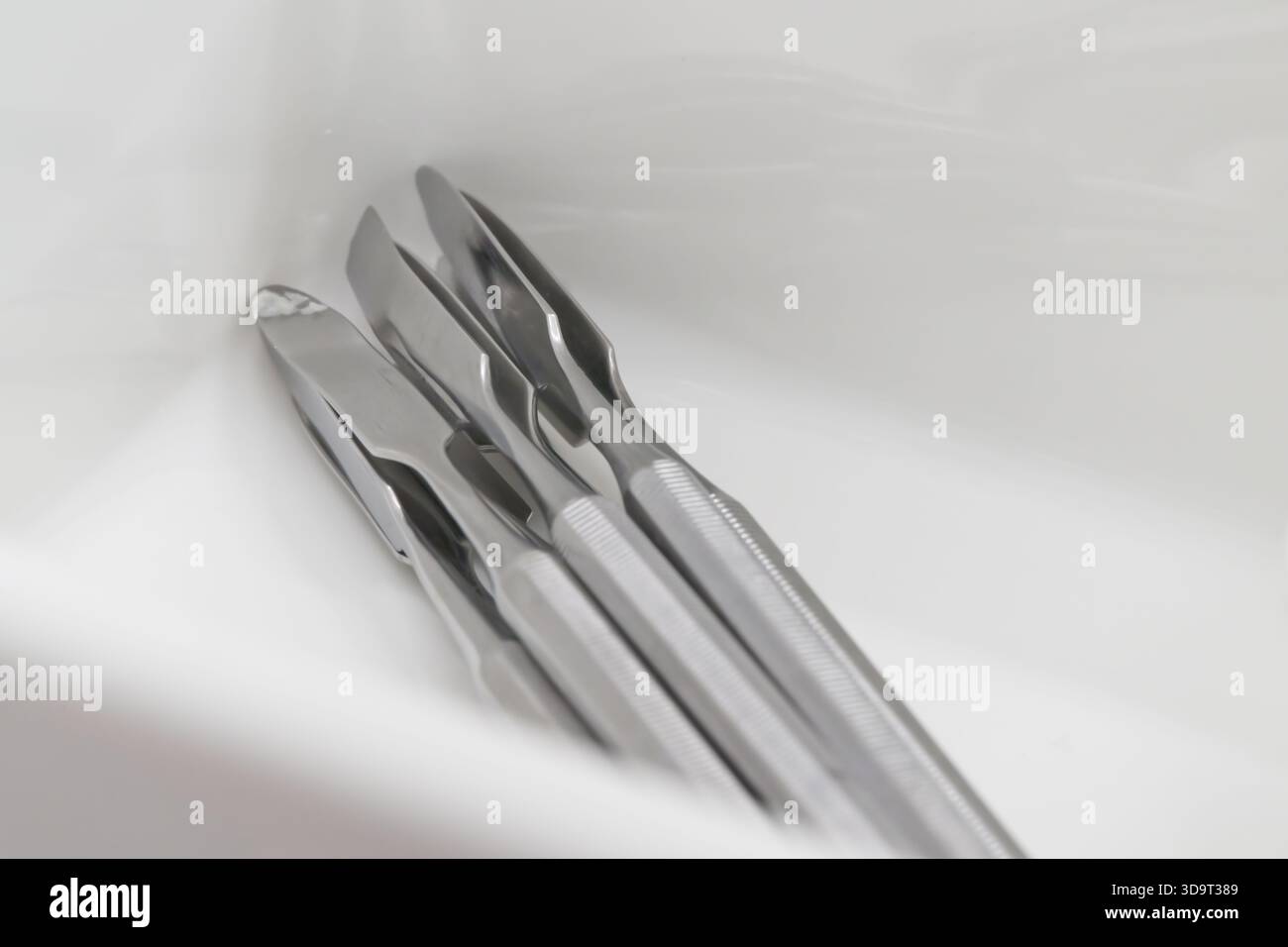 Vista ravvicinata di tre strumenti chirurgici in acciaio inox collocati in un contenitore bianco. Gli strumenti hanno una finitura lucida e sono disposti in modo ordinato Foto Stock