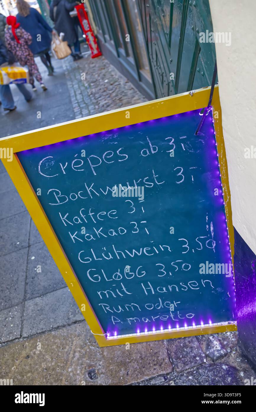 Un colorato menu di lavagna esposto all'esterno di un negozio, con vari cibi e bevande a prezzi. Tra i prodotti sono inclusi crêpes, bockwurst, caffè, caldo Foto Stock
