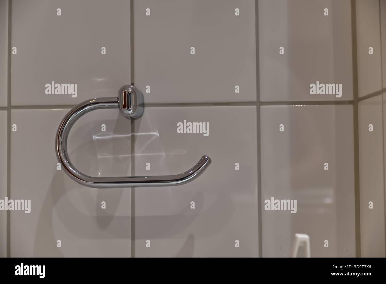 Vista ravvicinata di un portasciugamani cromato montato su una parete piastrellata. Il supporto presenta un design elegante e moderno con una finitura lucida che riflette la luce. Foto Stock