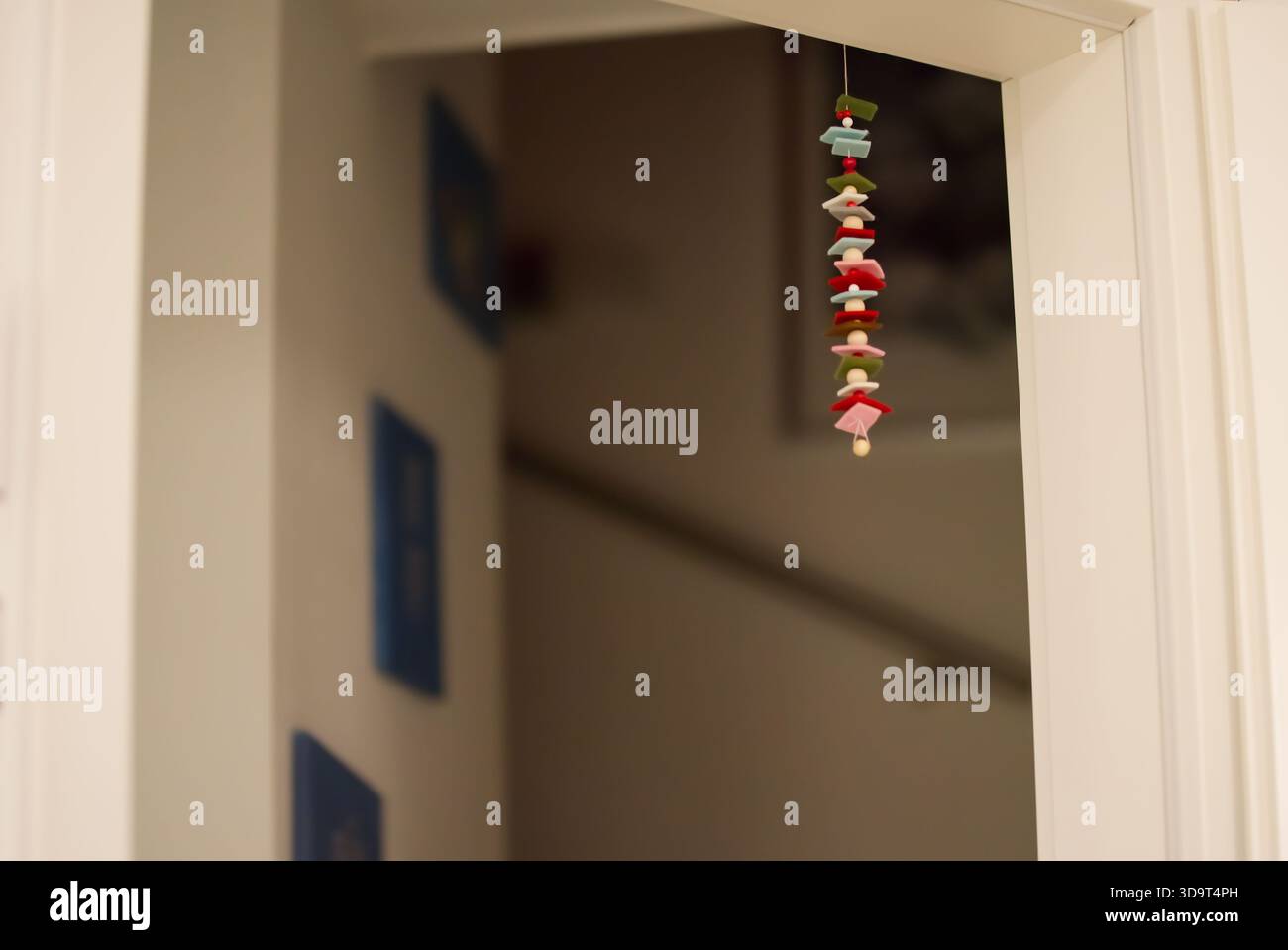 Un ornamento decorativo sospeso fatto di figure colorate, sospese da una porta. Lo sfondo presenta una scala sfocata e pareti d'arte blu. Foto Stock