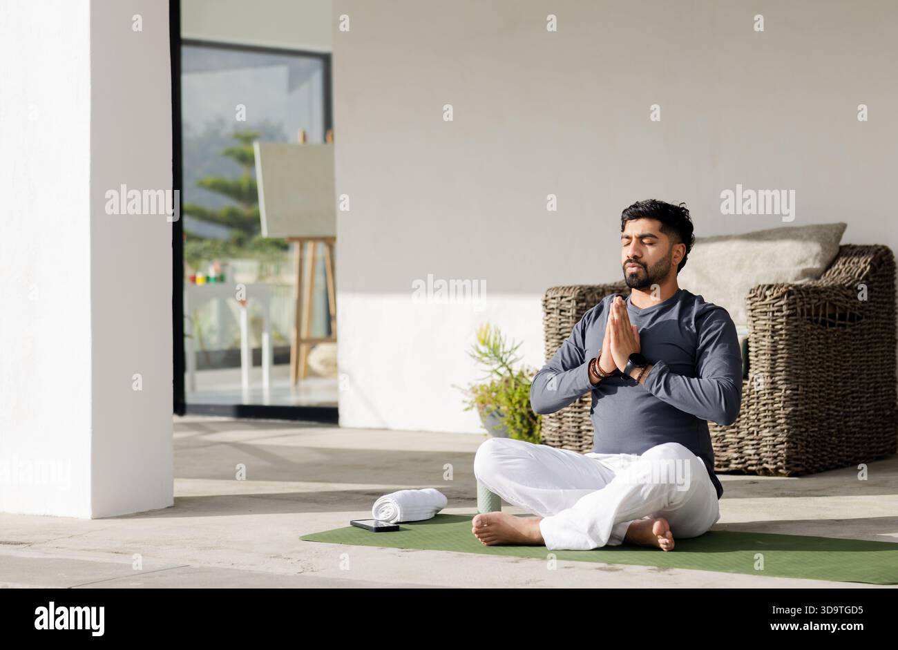 Uomo indiano che meditava sul tappetino da yoga con asciugamano, tavoletta, cavalletto sul patio, spazio fotocopie Foto Stock