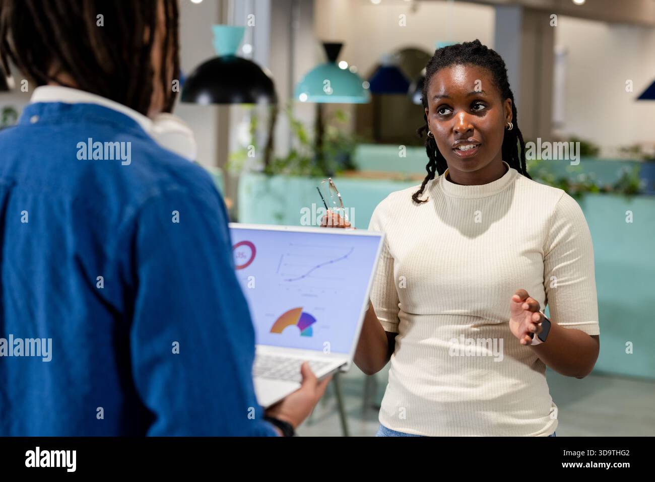 Colleghi afroamericani che discutono di carte dei laptop mentre una donna tiene gli occhiali in un ufficio aperto Foto Stock
