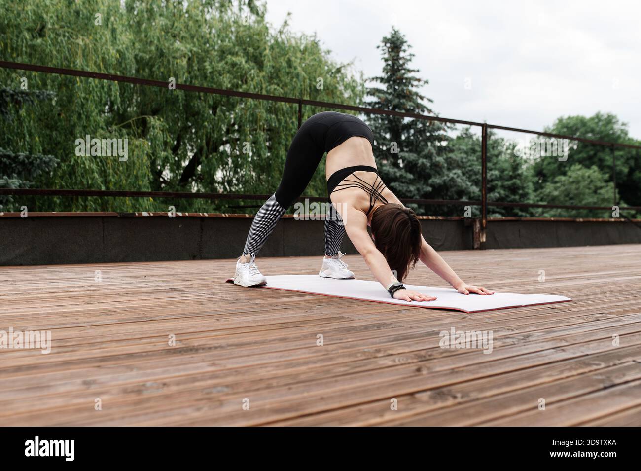 Donna sportiva e simpatica con capelli corti che pratica yoga all'aperto su un ponte di legno. Foto Stock