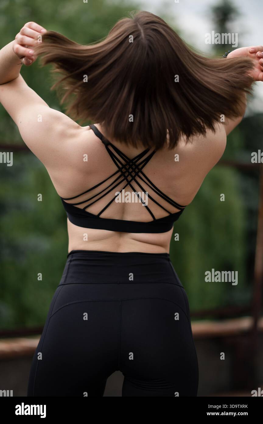 Attraente donna per il fitness con capelli corti in abbigliamento sportivo che si allunga all'aperto, vista posteriore. Foto Stock