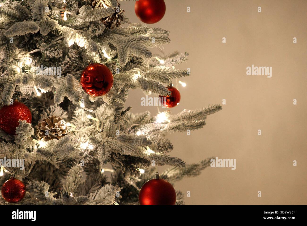 Bellissimo albero di Natale innevato con luci accese e ornamenti rossi, perfetto per temi di calore, celebrazione e fascino delle vacanze. Foto Stock