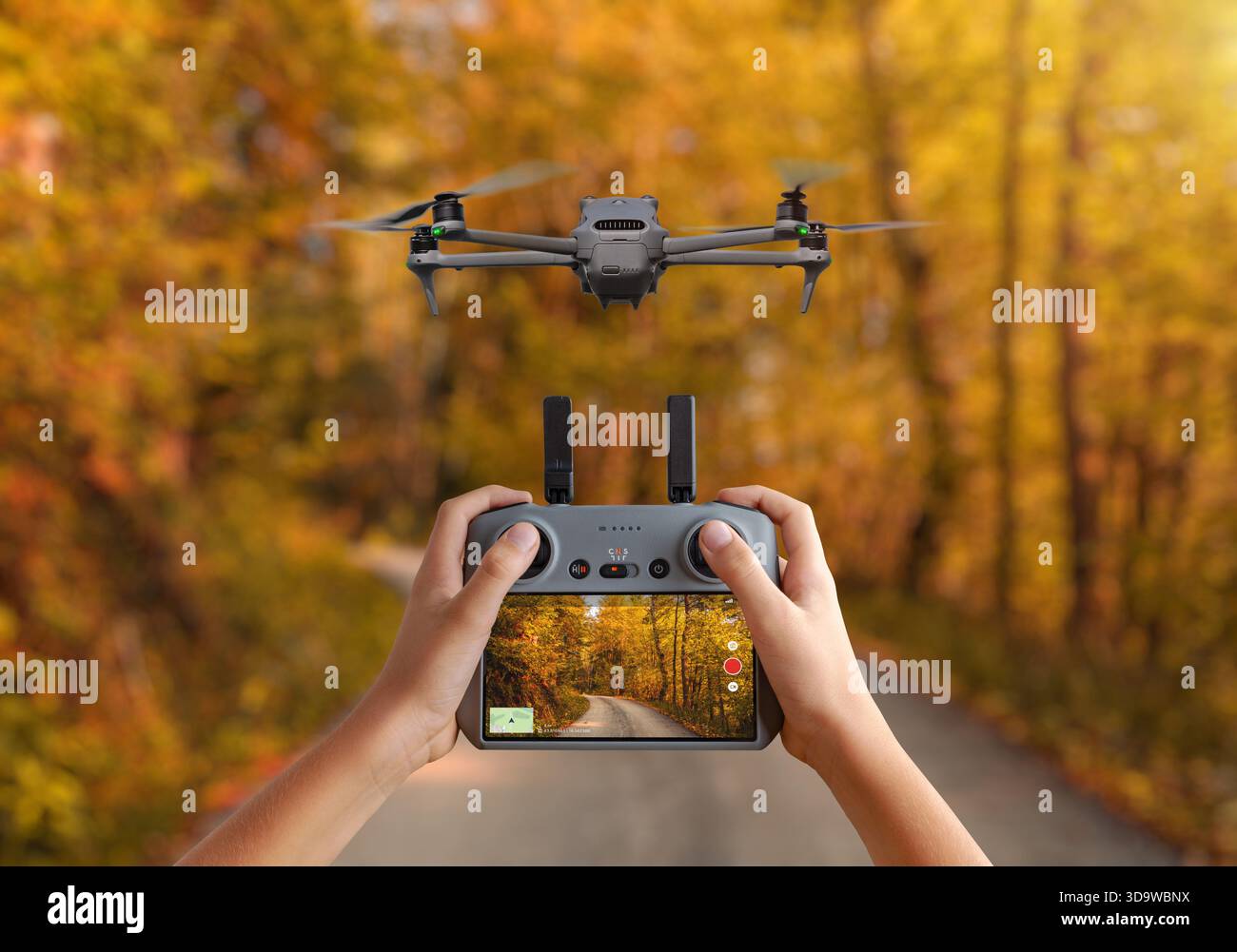 Drone aereo sorvolato sopra una strada forestale autunnale, controllato da un telecomando portatile che visualizza un feed video in diretta per le riprese e il monitoraggio Foto Stock