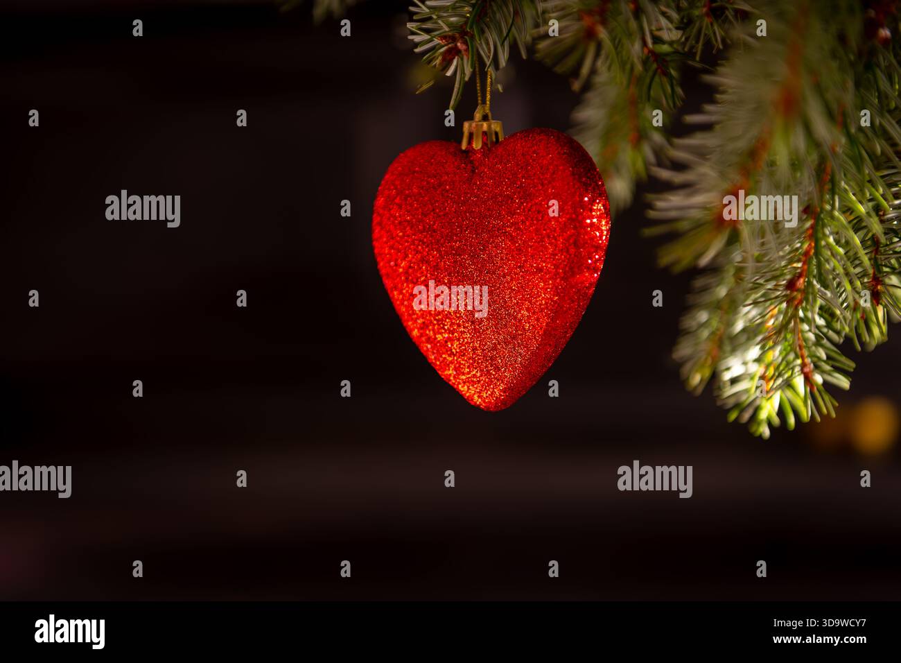 Un primo piano di una pallina di Natale rossa a forma di cuore appesa su un albero di Natale su uno sfondo scuro. Uno sfondo di elementi natalizi. Foto Stock