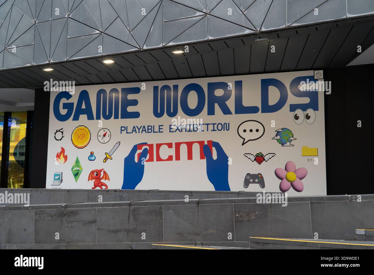 Un grande banner colorato che promuove la mostra giocabile Game Worlds presso ACMI, decorato con varie illustrazioni a tema di gioco. Foto Stock