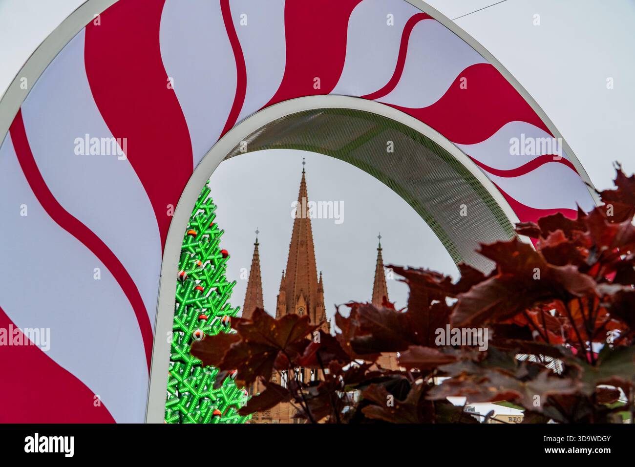 Un festoso arco rosso e bianco incornicia un vibrante albero di Natale verde, guglie storiche della cattedrale e fogliame rosso fuori dal fuoco. Foto Stock