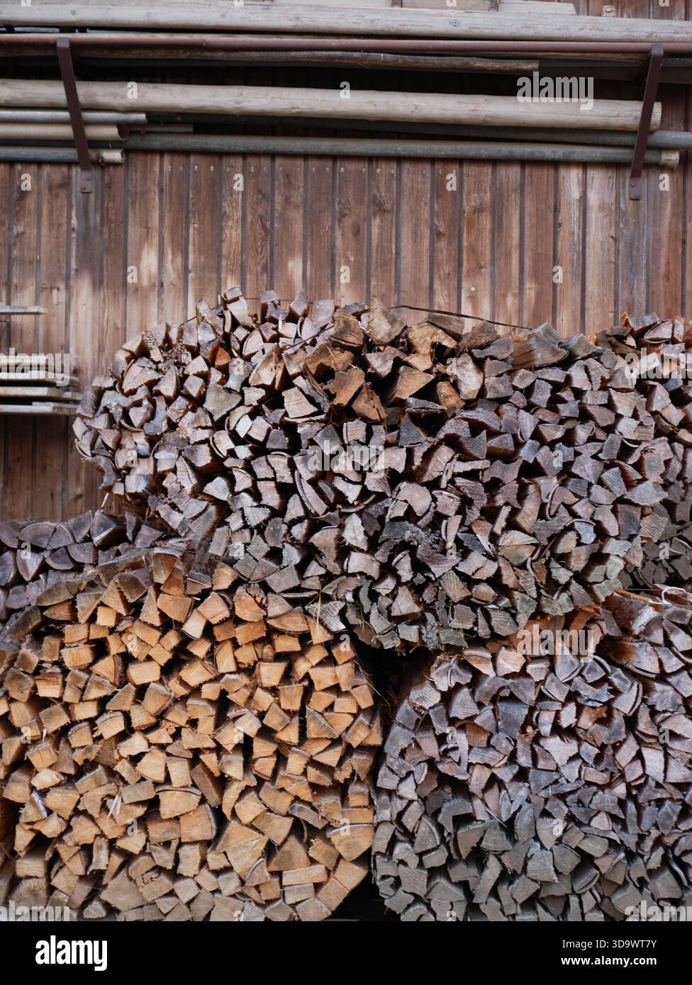 Tronchi di legna da ardere impilati ordinatamente su pareti in legno rustico in capannone di stoccaggio all'aperto, pronti per il riscaldamento invernale, evocando una vita rurale accogliente e sostenibile Foto Stock