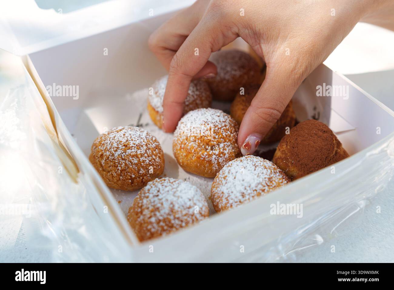 Primo piano della mano selezionando una sfoglia con crema di choux dal set di confezioni da forno con una varietà di gusti Foto Stock