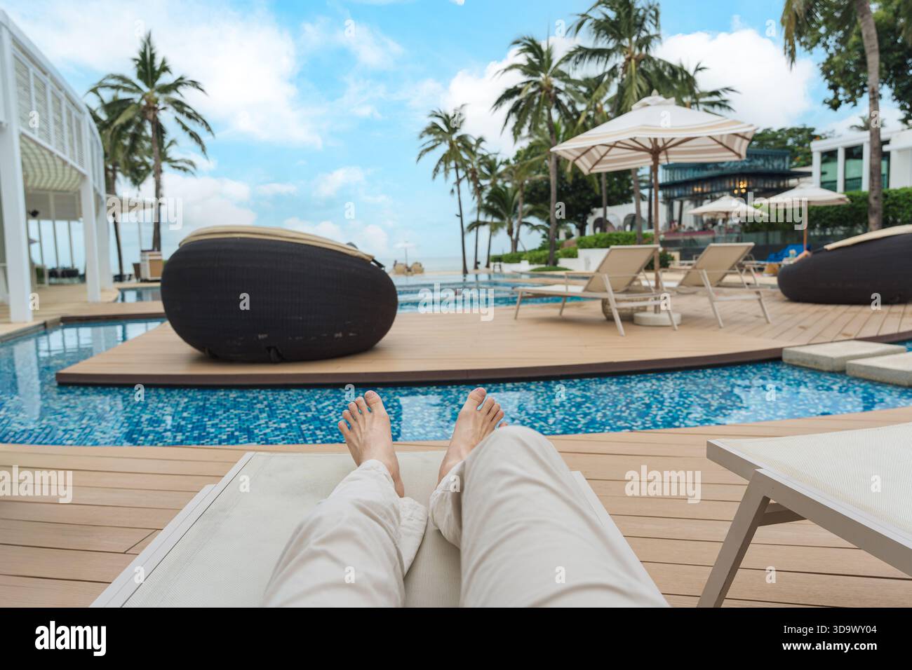 Persona che si rilassa sulla poltrona e a bordo piscina nel resort tropicale al banco durante il fine settimana Foto Stock
