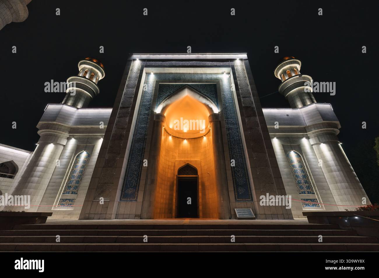 Moschea centrale con ingresso illuminato e minareti simmetrici di architettura islamica di notte ad Almaty, Kazakistan Foto Stock