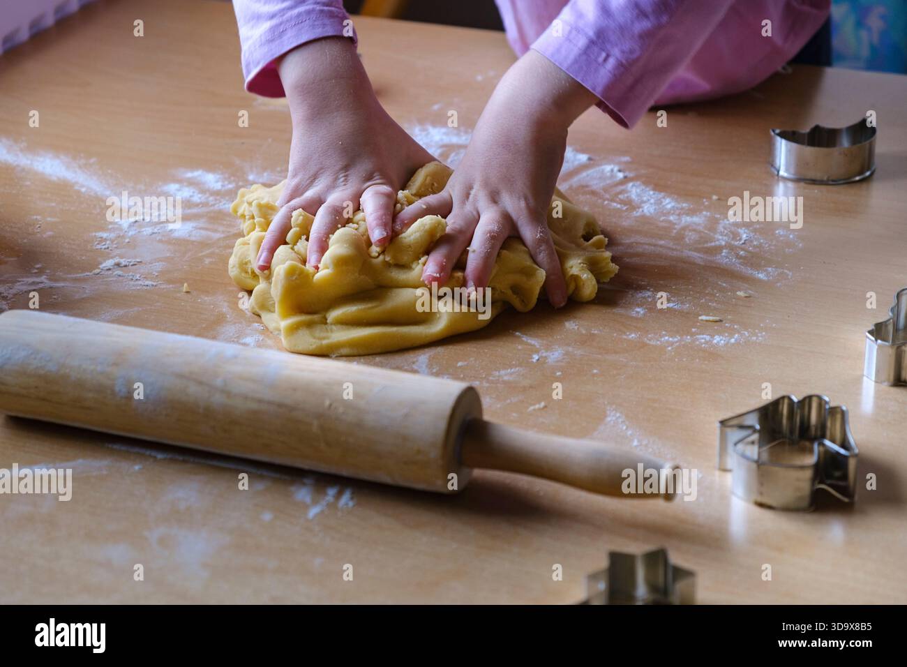 Le piccole mani premono e impastano l'impasto con un mattarello e dei taglierini nelle vicinanze. Cottura al tatto. Foto Stock