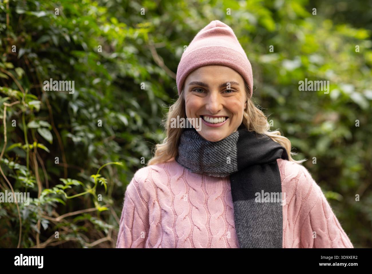 Donna in piedi sul percorso del parco con berretto rosa, maglione a maglia a cavo e sciarpa grigia e nera Foto Stock
