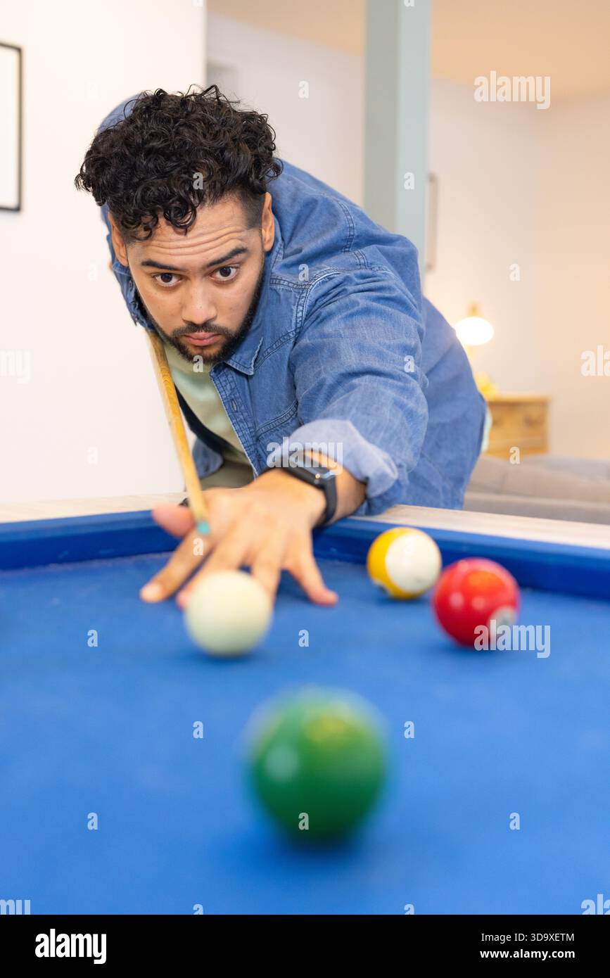 Uomo che si appoggia sul tavolo da biliardo nella sala giochi e mira la palla con un bastoncino tra le palle Foto Stock