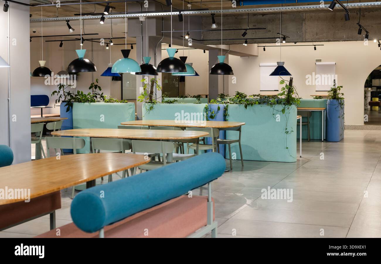 La piantatrice turchese-menta divide zone lounge di coworking e incornicia tavoli di legno con piante Foto Stock