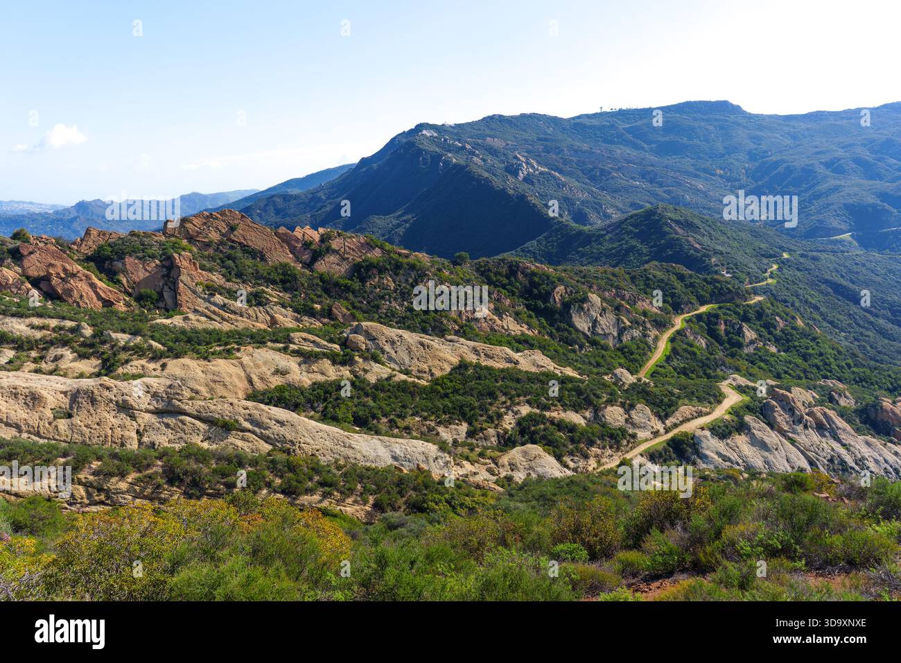 La tortuosa strada sterrata si snoda attraverso le aspre montagne della California meridionale, rivelando impressionanti formazioni rocciose e lussureggianti cappelle verdi sotto un blu chiaro Foto Stock