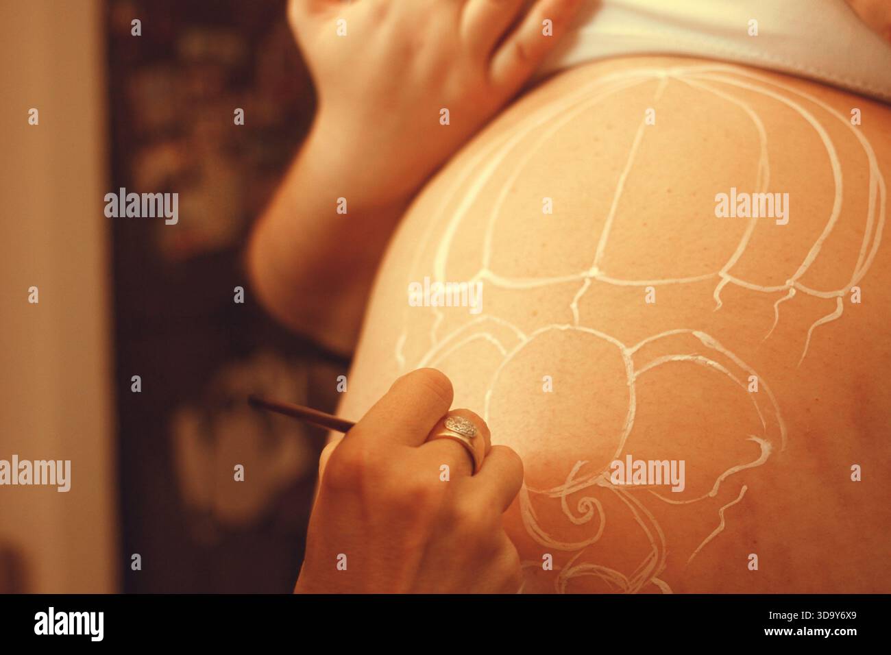 Donna incinta che fa applicazione con un professionista del corpo pittore , pittura del corpo sulla sua pancia con il pennello Foto Stock