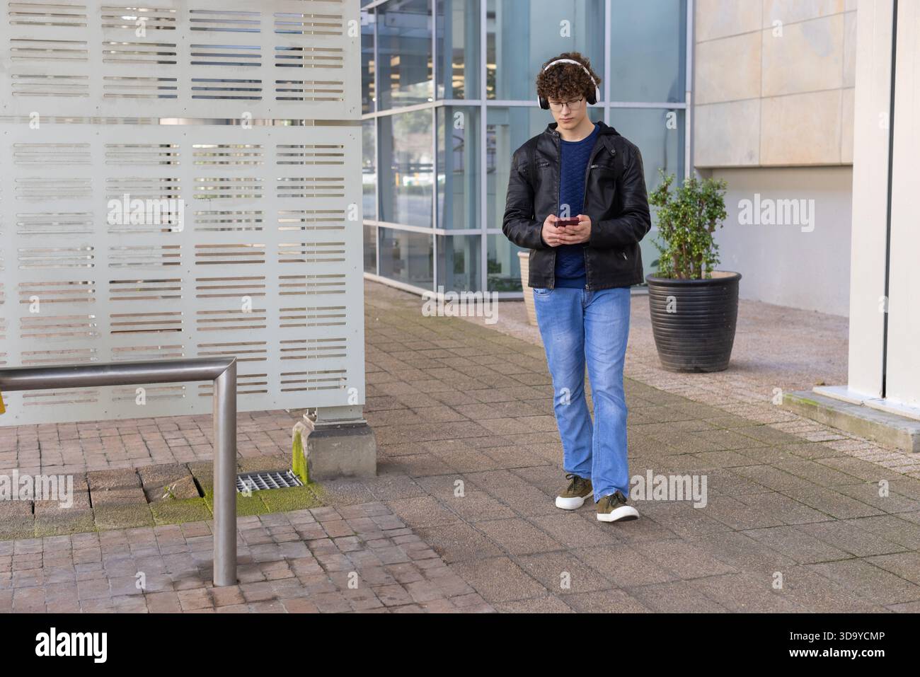 Uomo che cammina su asfaltatrici di mattoni accanto al pannello a strisce utilizzando smartphone e cuffie, spazio di copia Foto Stock