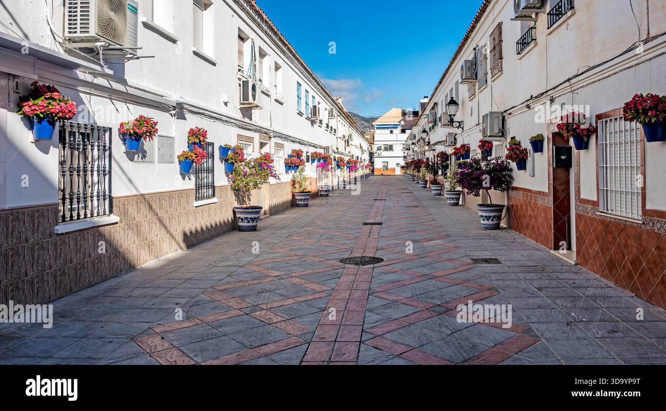 Una strada stretta e soleggiata a Fuengirola, fiancheggiata da tradizionali edifici andalusi bianchi e decorata con vivaci gerani in pentole di ceramica blu. Foto Stock