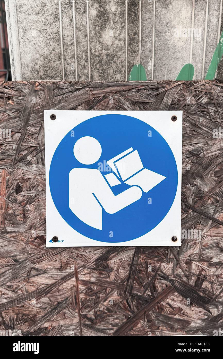 Segnale di sicurezza obbligatorio che mostra il manuale di istruzioni per la lettura del lavoratore su pareti in legno scheggiato in cantiere o in cantiere industriale. Foto Stock