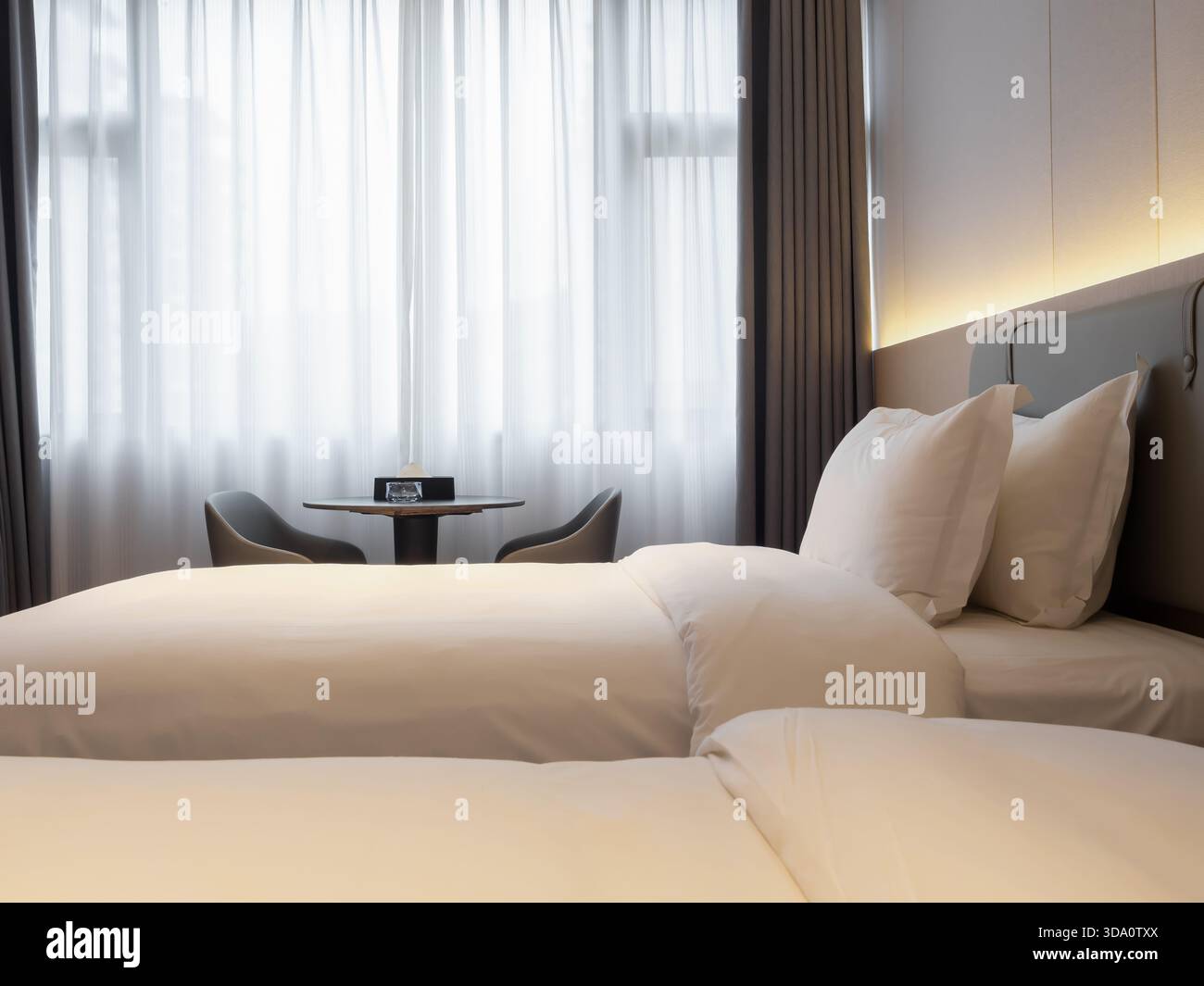 Camera da letto pulita con letti bianchi disposti in modo ordinato, illuminazione soffusa e atmosfera tranquilla, ideale per concetti di relax, comfort, Foto Stock