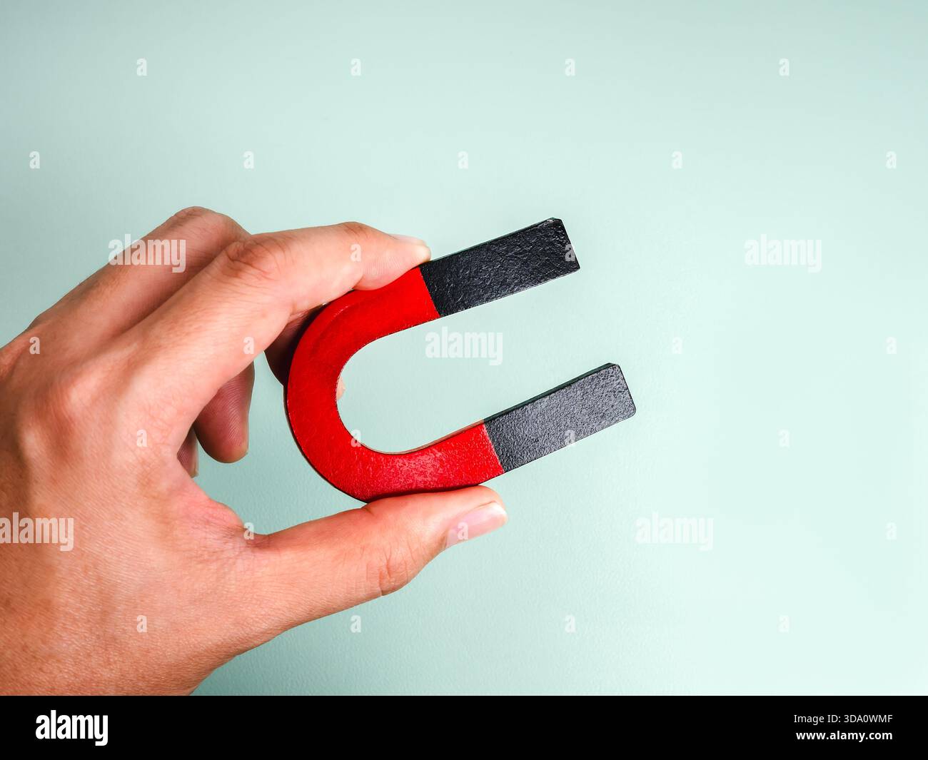 Magnete a ferro di cavallo rosso e nero isolato su sfondo verde pastello, simboleggia l'attrazione, il coinvolgimento del cliente, il branding personale e il m Foto Stock