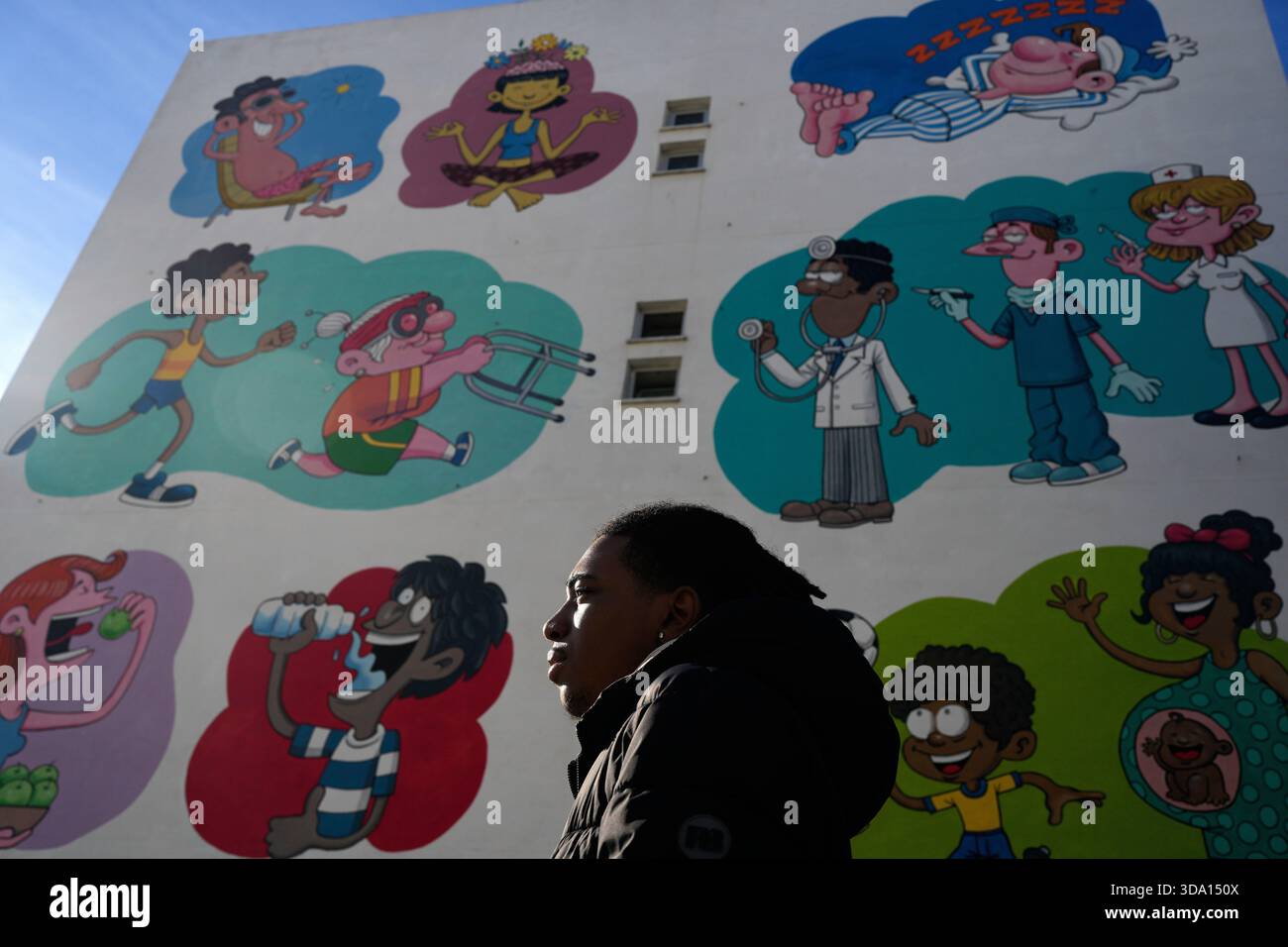 Vitor Tcheza Monteiro, a 16-year-old local resident training to become a tour guide, stands next to a mural by artist Pedro Ribeiro Ferreira, inspired by the United Nations Sustainable Development Goal 3, Good Health and Well-being, at the housing project Zambujal in Amadora, on the outskirts of the Portuguese capital Lisbon, Thursday, Nov. 27, 2025. (AP Photo/Armando Franca) Foto Stock