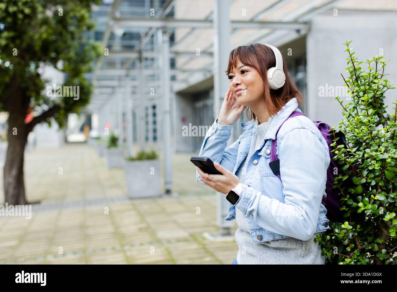 Donna asiatica che ascolta la musica sullo smartphone e regola le cuffie nel cortile, copia spazio Foto Stock