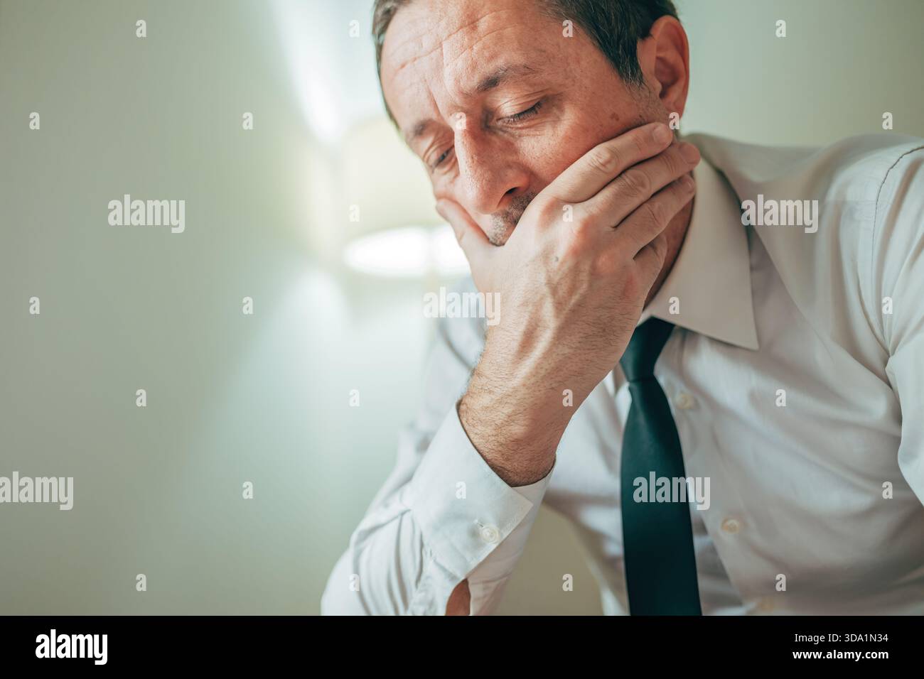 Stanco uomo d'affari che sbadiglia con la mano che copre la bocca, mostrando stanchezza e mancanza di sonno. Messa a fuoco selettiva. Foto Stock
