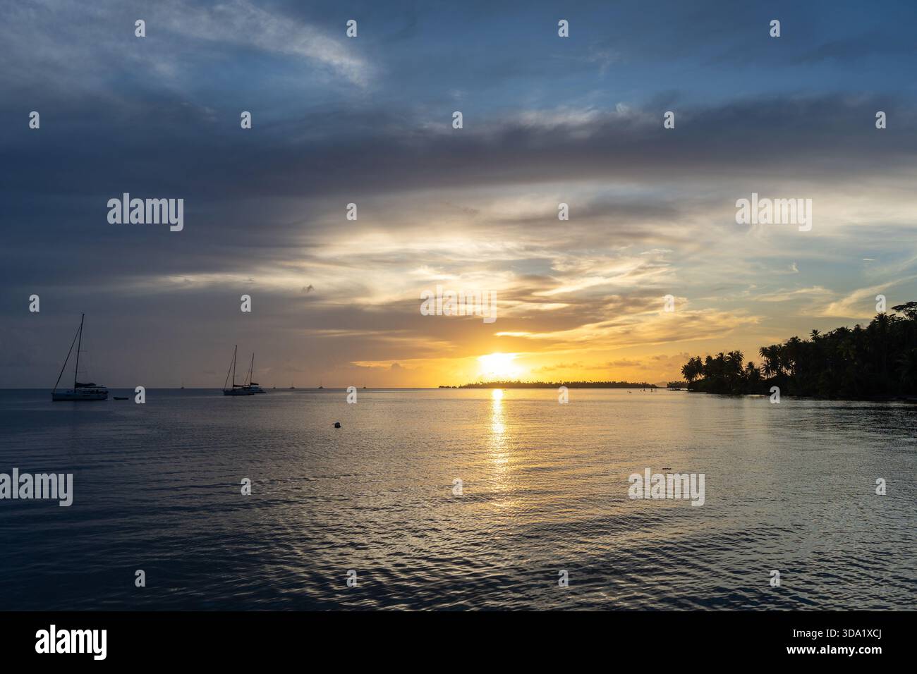 Uno splendido tramonto sull'isola di Tahaa nella Polinesia francese, con acque calme e barche a vela che creano un'atmosfera serena Foto Stock
