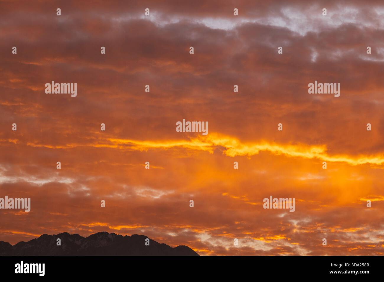 Il vivace tratto arancione attraversa il cielo al tramonto sopra le montagne. Foto Stock
