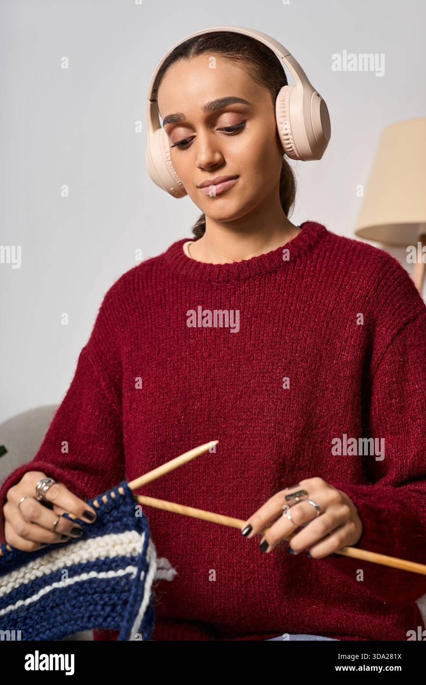 Una giovane donna ama lavorare a maglia indossando un maglione marrone nel suo elegante spazio abitativo. Foto Stock