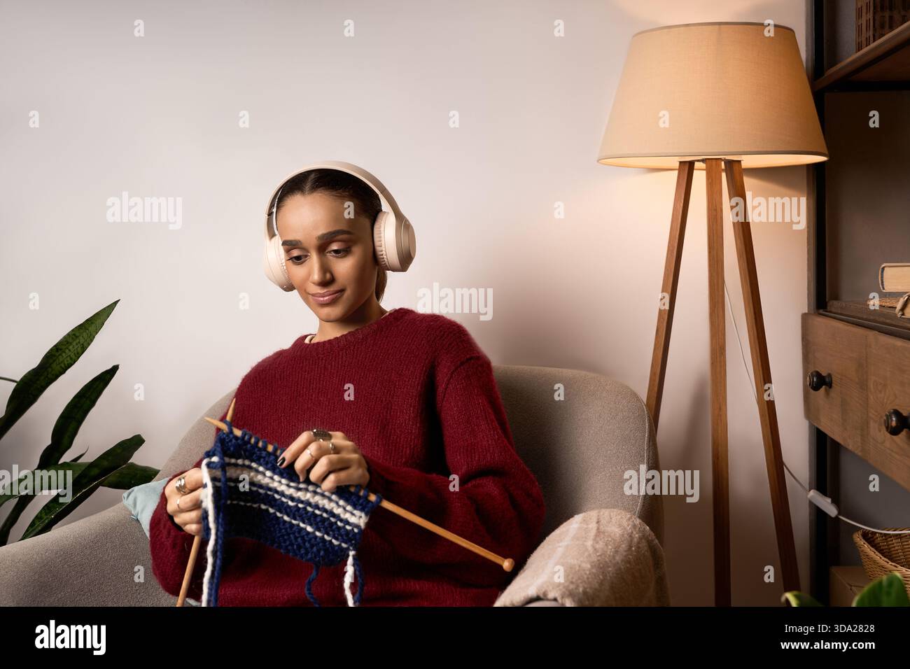 La giovane donna afroamericana ama trascorrere un pomeriggio rilassante a maglia a casa, indossando un maglione marrone. Foto Stock