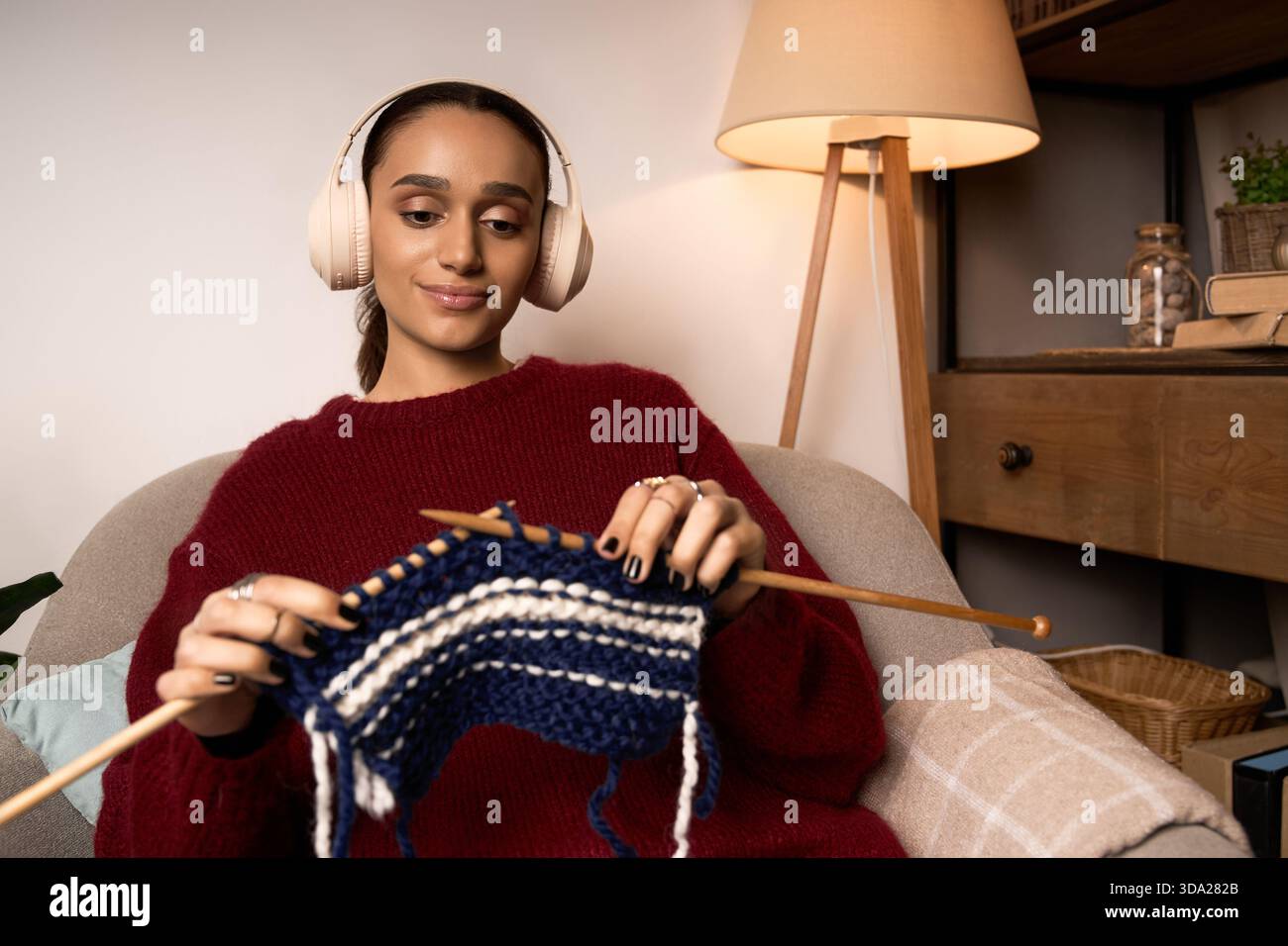 Una giovane donna ama lavorare a maglia nella sua casa elegante mentre ascolta la musica. Foto Stock