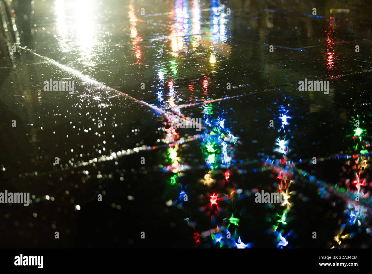 Luci di natale blu, verdi e rosse riflesse su un marciapiede in una notte piovosa Foto Stock