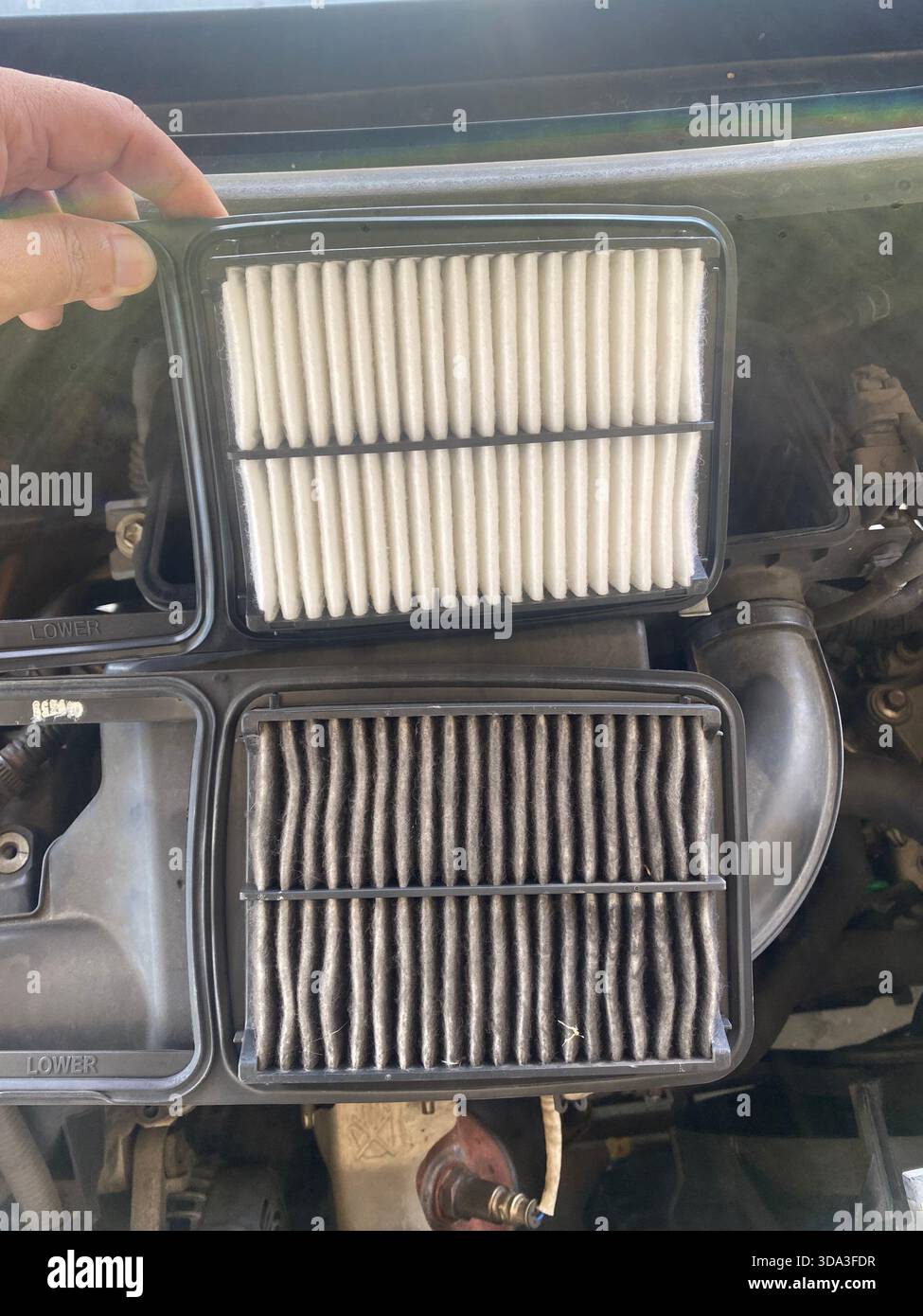Confronto tra un filtro dell'aria pulito e un filtro dell'aria sporco all'interno del vano motore di un veicolo durante la manutenzione. - Immagine stock catturata con smartphone